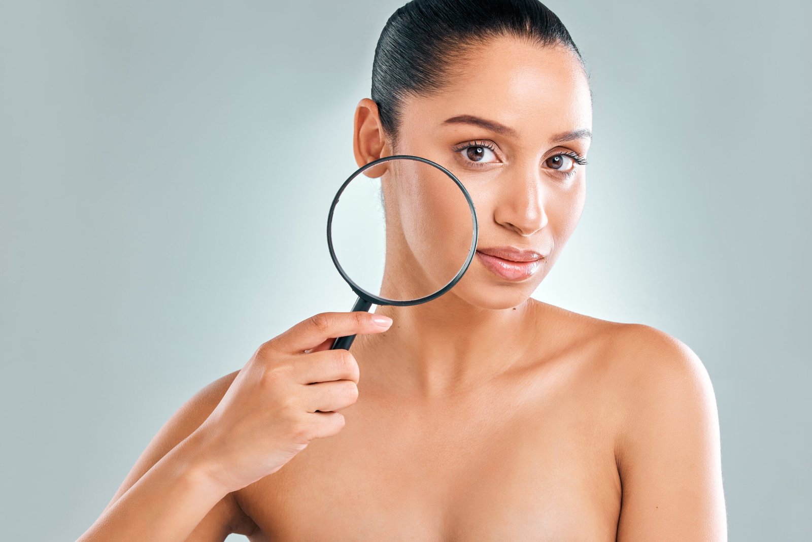 Studio shot of an attractive young woman looking through a magnifying glass against a grey background